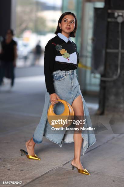 Fashion Week guest is seen wearing a black pullover with shapes in sequins, underneath a blue shirt, a denim midi skirt with front split, a orange...