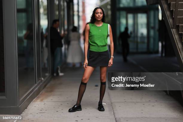Fashion Week guest is seen wearing a golden necklace with a cross, a green tank top, a black mini skirt, a mint leather bag, a silver watch, golden...