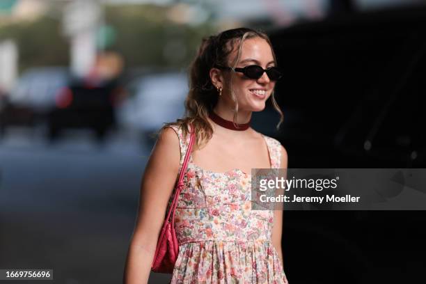 Fashion Week guest is seen wearing black sunglasses, silver hoop earrings, a dark red choker, a white/pink/lilac/green/yellow midi dress with floral...