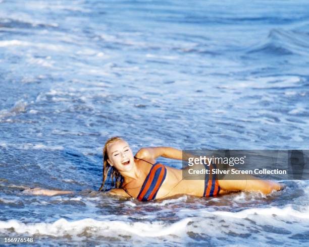 German actress Elke Sommer wearing a bikini as she lies in the surf at a beach, circa 1965.