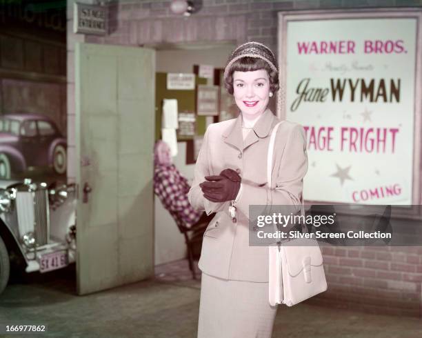 American actress and singer Jane Wyman standing next to a poster for her latest film, Alfred Hitchcock's 'Stage Fright', 1950.