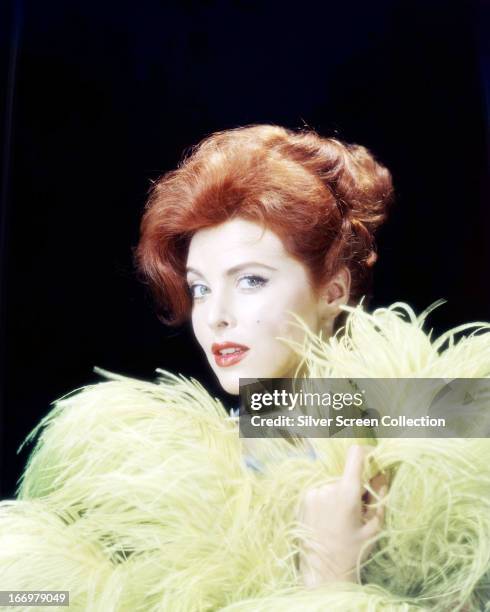 American actress Tina Louise, posing with yellow ostrich feathers, circa 1960.