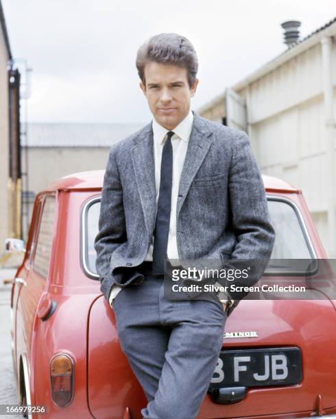 American actor Warren Beatty posing by a red Mini car in a promotional portrait for 'Kaleidoscope', directed by Jack Smight, 1966.