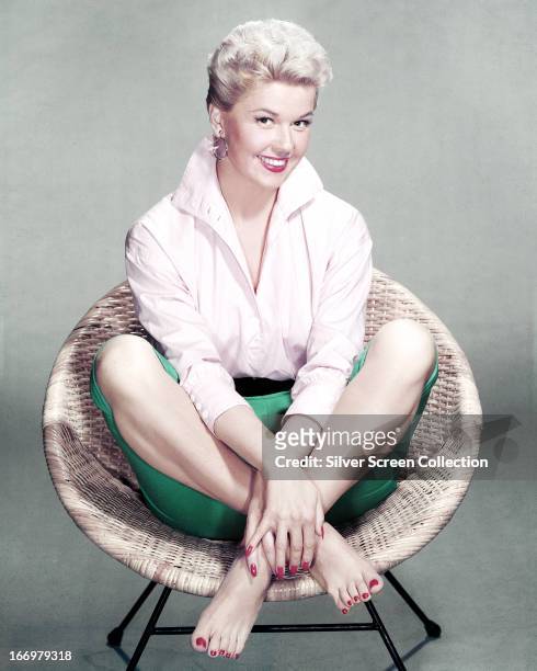 American actress and singer Doris Day sits cross-legged and barefoot in a rattan chair, circa 1955.
