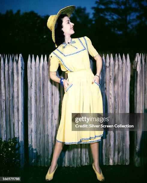 American actress Joan Bennett in a yellow sun dress with blue and purple trim and a matching sun hat, circa 1935.