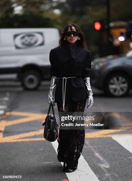 Fashion Week guest is seen wearing big silver hoop earrings, black sunglasses from Celine, a long black blazer with a rhinestone ribbon as a belt,...