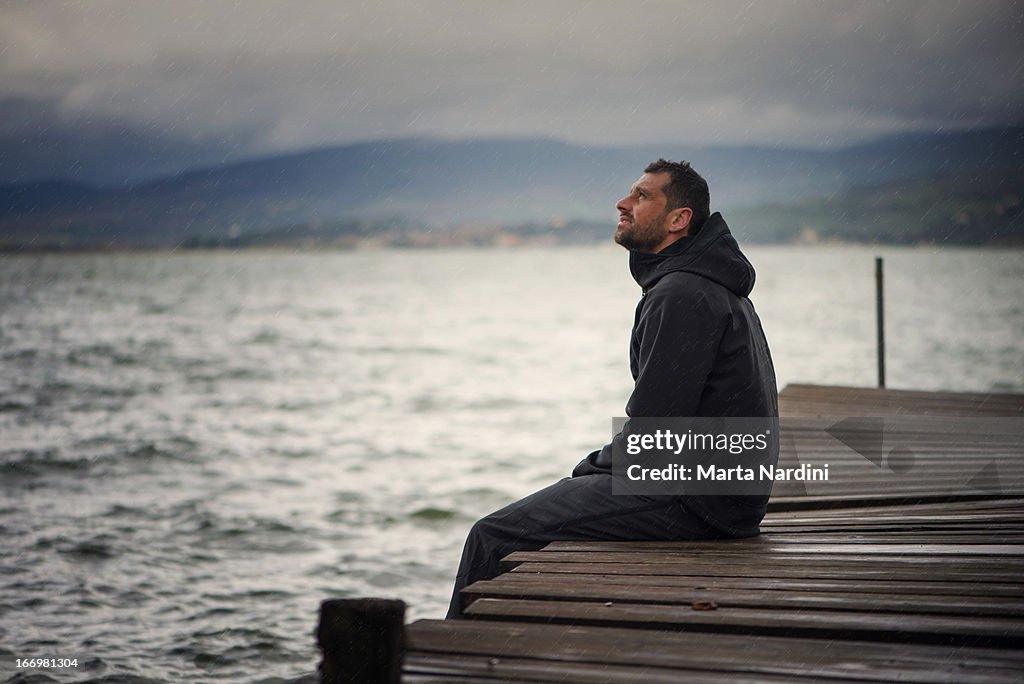 Lonely man sitting on pier under rain