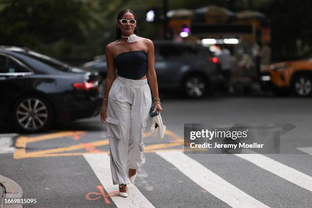 Fashion Week guest is seen wearing silver hoop earrings, a white satin choker with a big rose, a pinstriped black strapless top, beige cargo pants,...