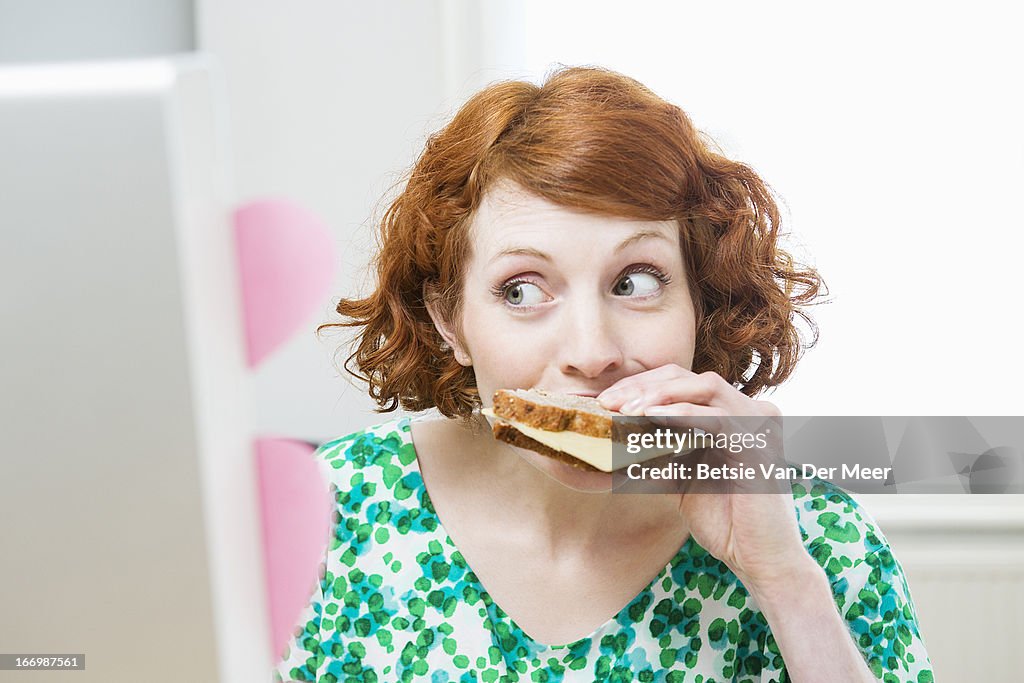 Woman eating sandwich while working on computer.