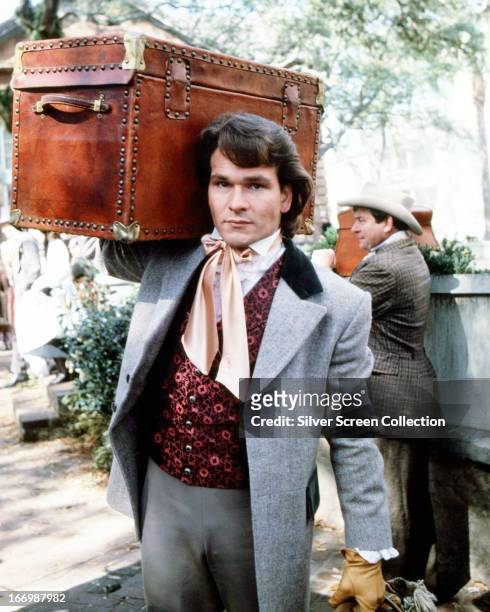 American actor Patrick Swayze carrying a trunk, as Orry Main in the TV miniseries 'North And South', 1985.