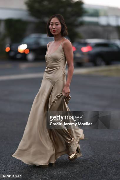Aimee Song is seen outside Ralph Lauren show wearing a golden necklace with a diamond, golden, flowing, silk, long Ralph Lauren dress without sleeves...