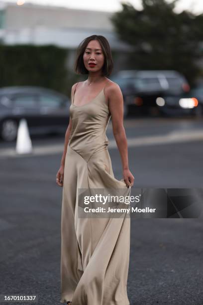 Aimee Song is seen outside Ralph Lauren show wearing a golden necklace with a diamond, golden, flowing, silk, long Ralph Lauren dress without sleeves...