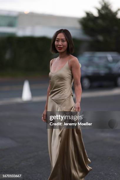 Aimee Song is seen outside Ralph Lauren show wearing a golden necklace with a diamond, golden, flowing, silk, long Ralph Lauren dress without sleeves...