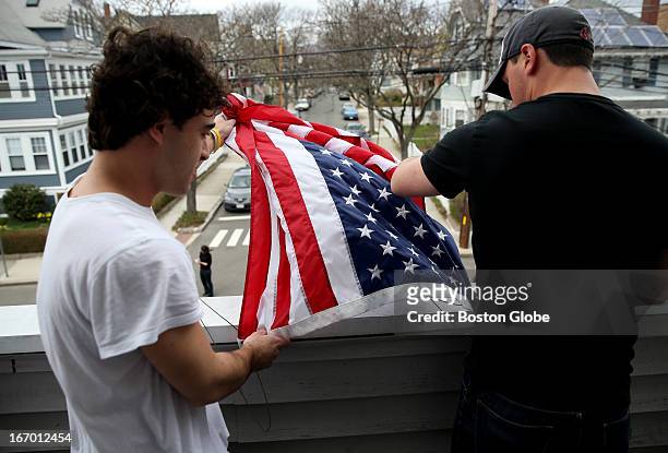 Tufts University students Thomas Isman, left, and Gary Grandonico, right, hang an American flag from the porch in honor of their neighbor, Sean...