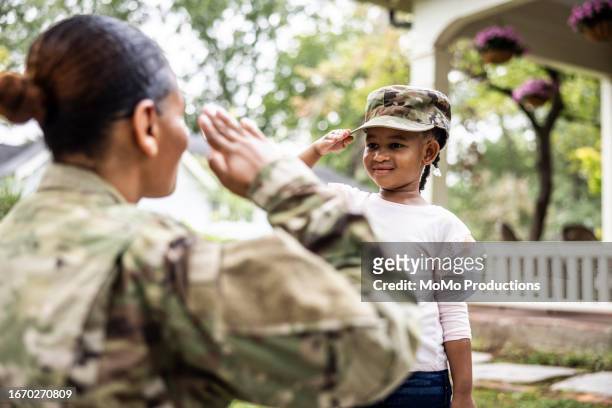 daughter saluting female u.s. soldier mother in front of home - kid power event in atlanta stock pictures, royalty-free photos & images