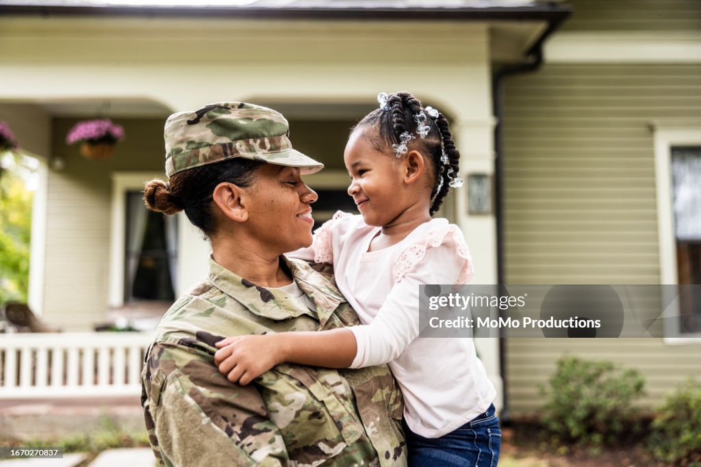 Portrait of female U.S. soldier in uniform with young daughter in front of home