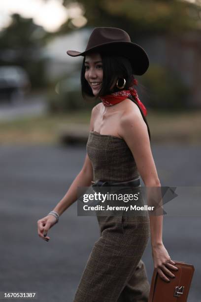 Is seen outside Ralph Lauren show wearing a full Ralph Lauren look, brown cowboy hat, red scarf piece around neck, brown checkered jumsuit with free...