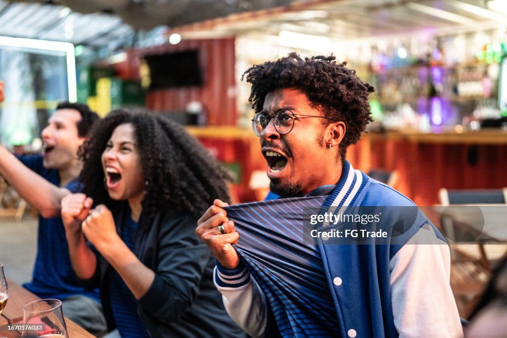 Sports fans watching a match and celebrating at bar