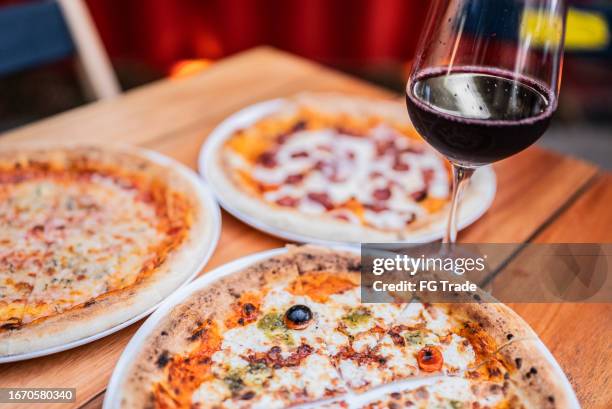 high angle view of pizzas and wineglass on table at pizzeria - pizzeria stockfoto's en -beelden