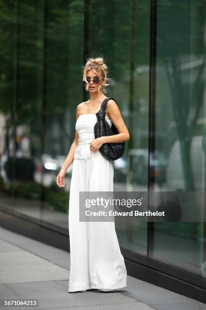 Xenia Adonts wears sunglasses, a large oversized Bottega Veneta bag, a white off-shoulder top, white pants, outside Proenza Schouler, during New York...
