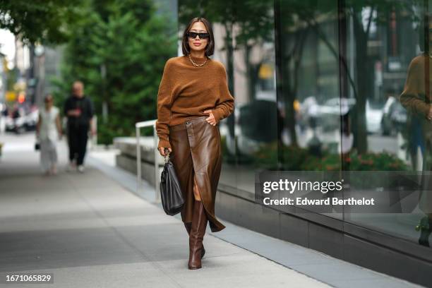 Aimee Song wears sunglasses, a necklace, a brown wool pullover, a brown leather skirt, a black leather bag, brown knee-high boots, outside Proenza...