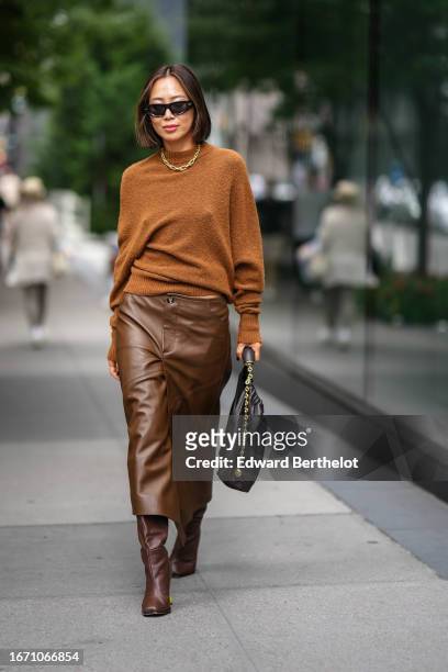 Aimee Song wears sunglasses, a necklace, a brown wool pullover, a brown leather skirt, a black leather bag, brown knee-high boots, outside Proenza...