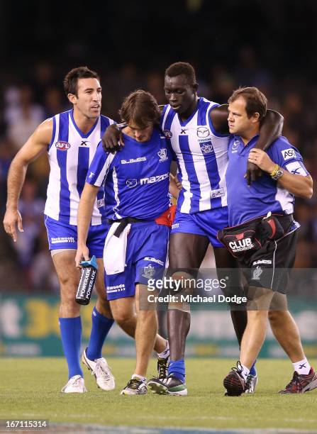 Majak Daw of the Kangaroos gets carried off the ground after a heavy knock as Michael Firrito lends his support during the round four AFL match...
