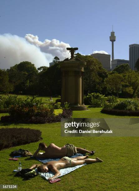 Couple sunbathe in Sydney's Royal Botanical Gardens as huge plumes of smoke sweep across the city, December 4, 2002 in Sydney, Australia. Over sixty...