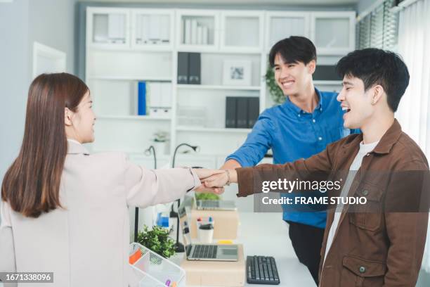 a diverse corporate team, including a confident asian businesswoman (30-34 years old) and her male colleague (25-29 years old), join hands in unity to celebrate their successful business strategy discussion in a modern, sustainable office. - 25 30 years old asian stock-fotos und bilder