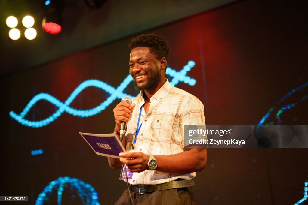 Speeker talking and showing a presentation to audience on stage with microphone