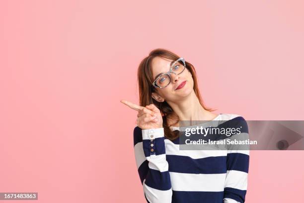 portrait of cheerful young woman over isolated pink background pointing finger to the side. - indicar fotografías e imágenes de stock