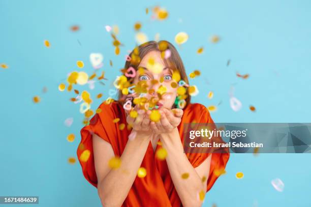 studio photo of young girl having fun while energetically blowing confetti on blue isolated background. concept of party and new year. - confetti light blue background stock pictures, royalty-free photos & images