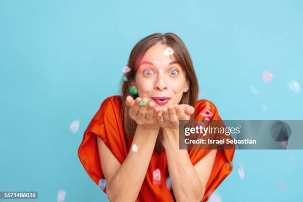 studio photo of young girl with blue eyes and party clothes having fun while energetically blowing confetti on blue isolated background. - confetti light blue background stock pictures, royalty-free photos & images