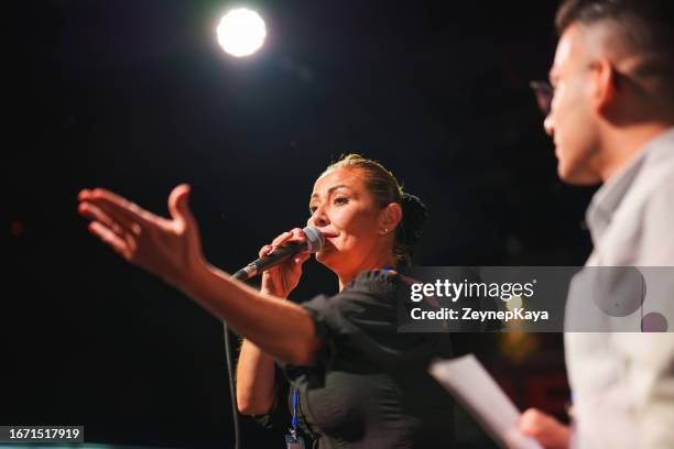 speeker talking and showing a presentation to audience on stage with microphone - women for women international gala stockfoto's en -beelden