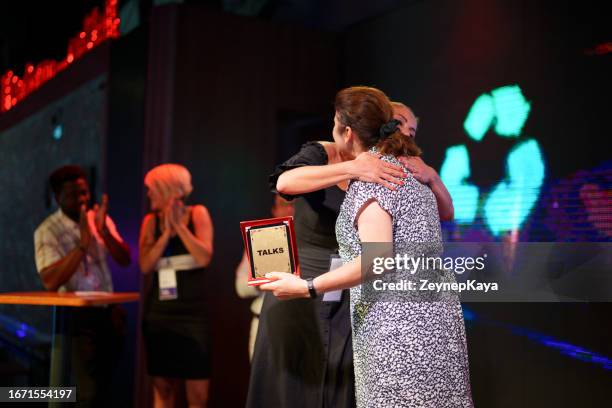 mid adult woman is receiving an award on stage for her speech - graduation podium stockfoto's en -beelden