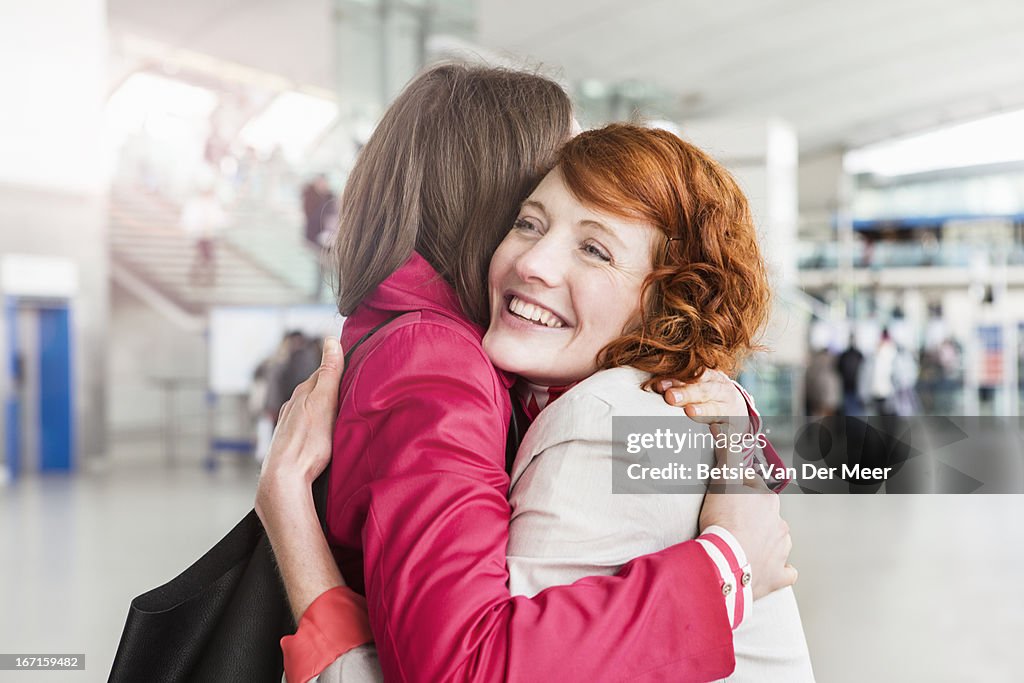 Women greeting, embracing, at arrival hall.