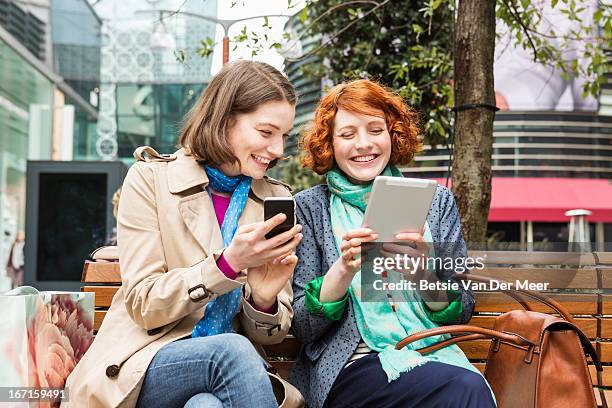 women laughing looking at wireless device. - young woman red hair urban stock pictures, royalty-free photos & images