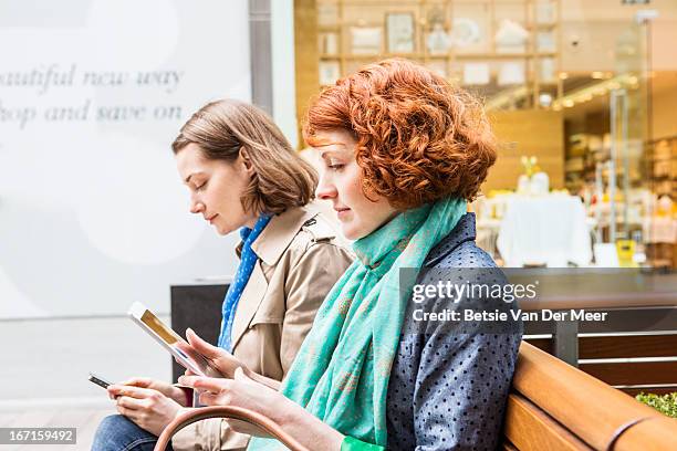 women sitting in shopping area looking at internet - two people side by side stock pictures, royalty-free photos & images