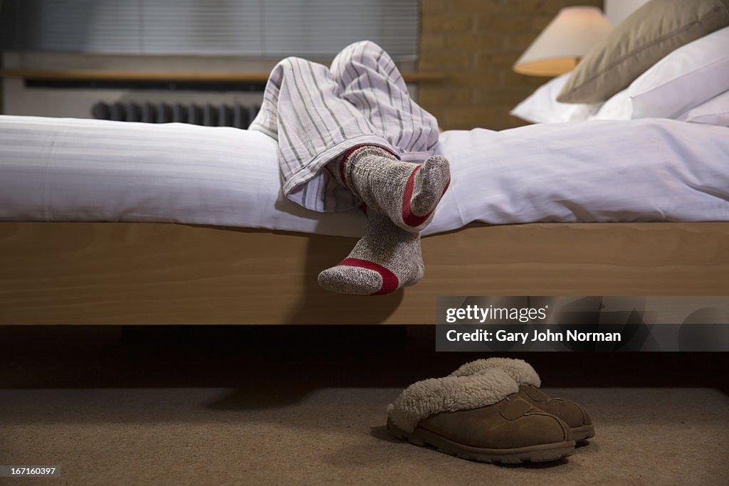 Womans legs wearing pyjamas hanging off bed