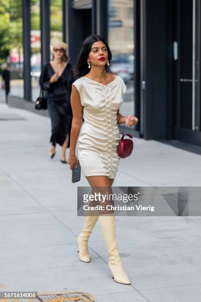 Guest wears creme white dress, boots, burgundy bag outside Bevza on September 09, 2023 in New York City.