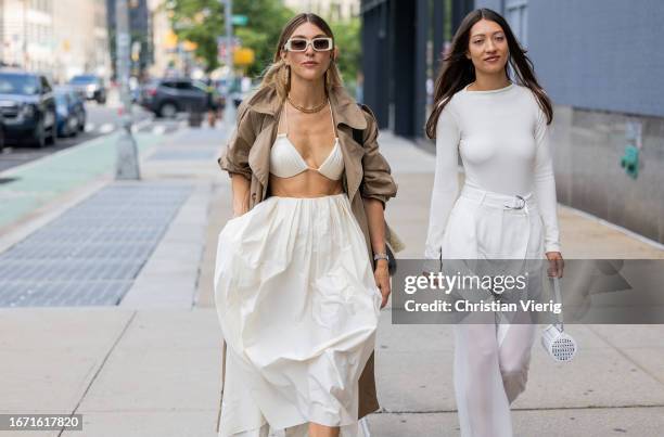 Guest wears white wide skirt, beige trench coat, black loafers & a guest wears white long shirt, transparent pants, bag outside Bevza on September...