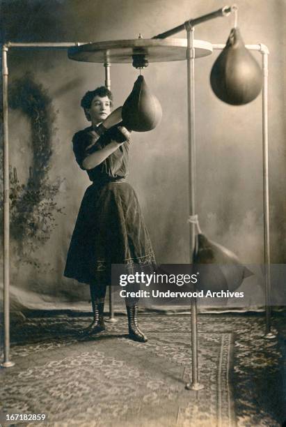 Young woman in a skirt working out with boxing gloves and a punching bag, 1890.