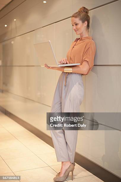 businesswoman using laptop in corridor - leaning stock pictures, royalty-free photos & images