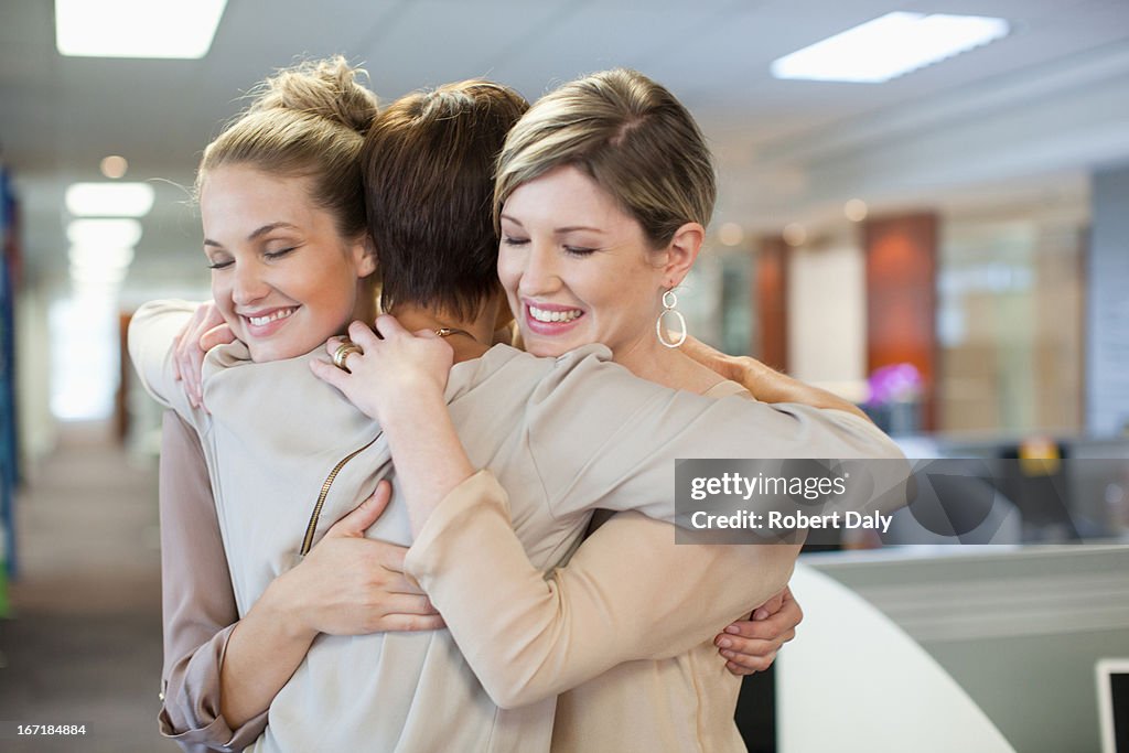 Mujeres de negocio feliz abrazándose en oficina