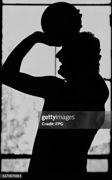 American basketball player Larry Bird, Celtics small forward, in silhouette with the ball raised above his head during a Boston Celtics training...