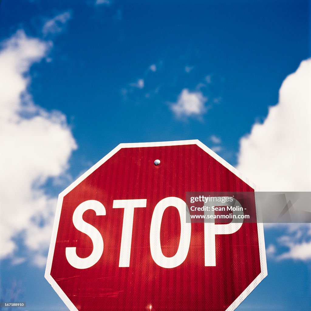 Stop sign against blue sky and puffy white clouds