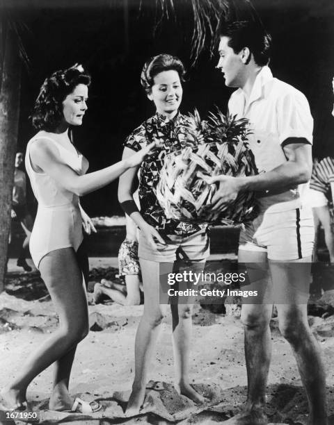 American singer and actor Elvis Presley holds a basket of pineapples in front of American actors Joan Blackman and Pamela Kirk in a still from the...