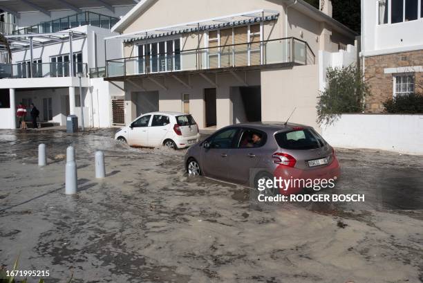 Cars drive across a street through seawater from unusually large waves in the coastal village of Gordon's Bay, South Africa on September 17, 2023...