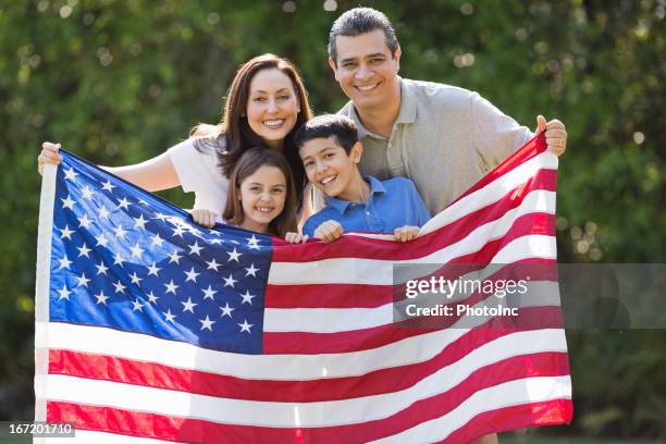 Familia Sonriendo Mientras Sostiene Bandera Estadounidense En El Parque, Foto de stock