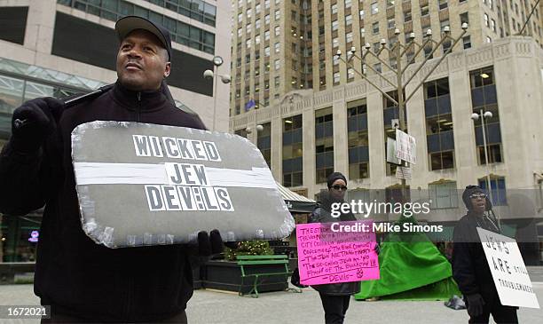 Protester Kubaka Oba , of the group the Black Fist, holds an anti-semitic sign in front of a menorah on Fountain Square December 4, 2002 in downtown...